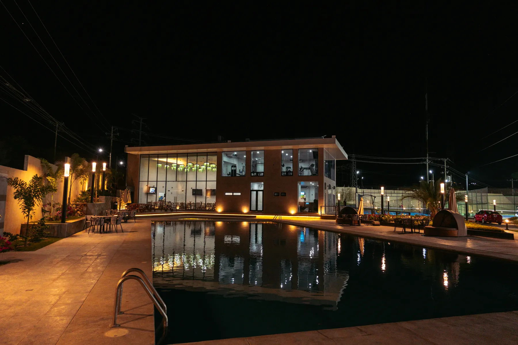Sport House de noche, con el gimnasio iluminado frente a la alberca